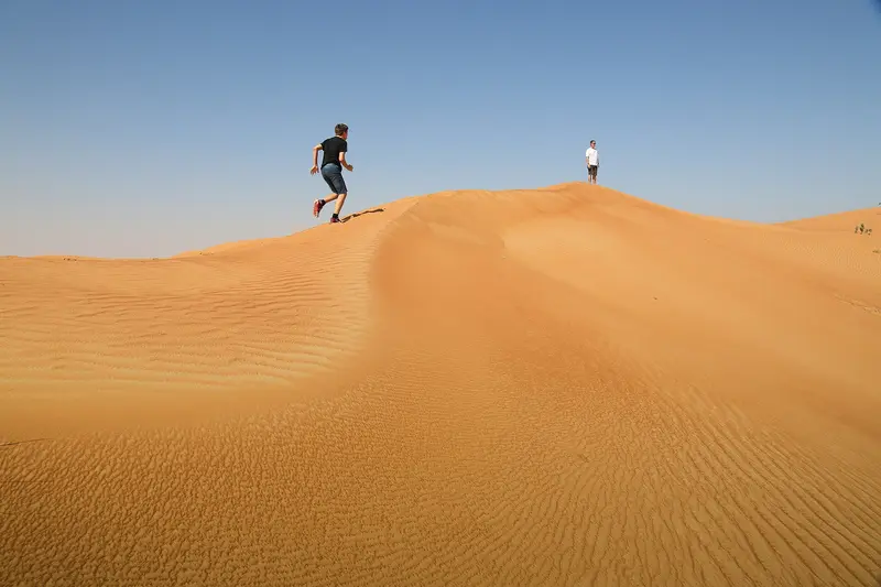 Two people crossing the crest of a dune in the UAE desert