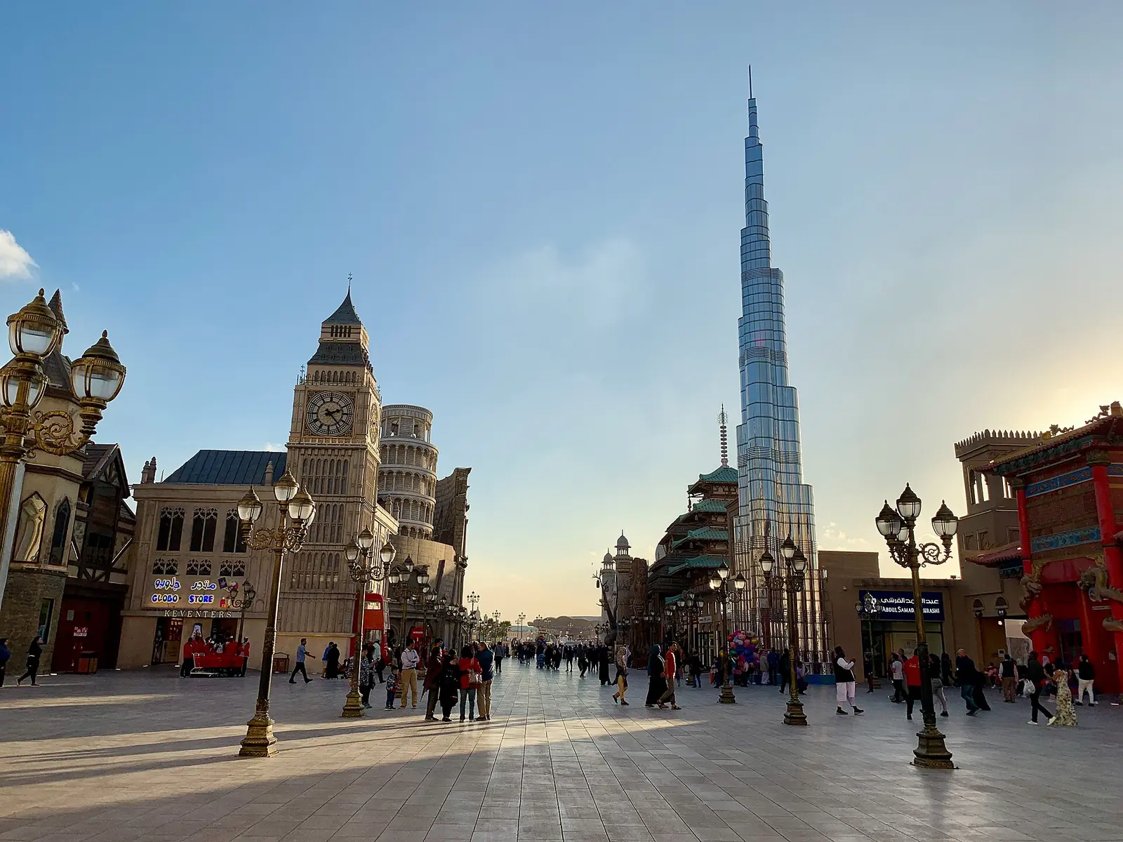 A plaza at Global Village in Dubai with the Burj Khalifa replica rising behind the pavilions